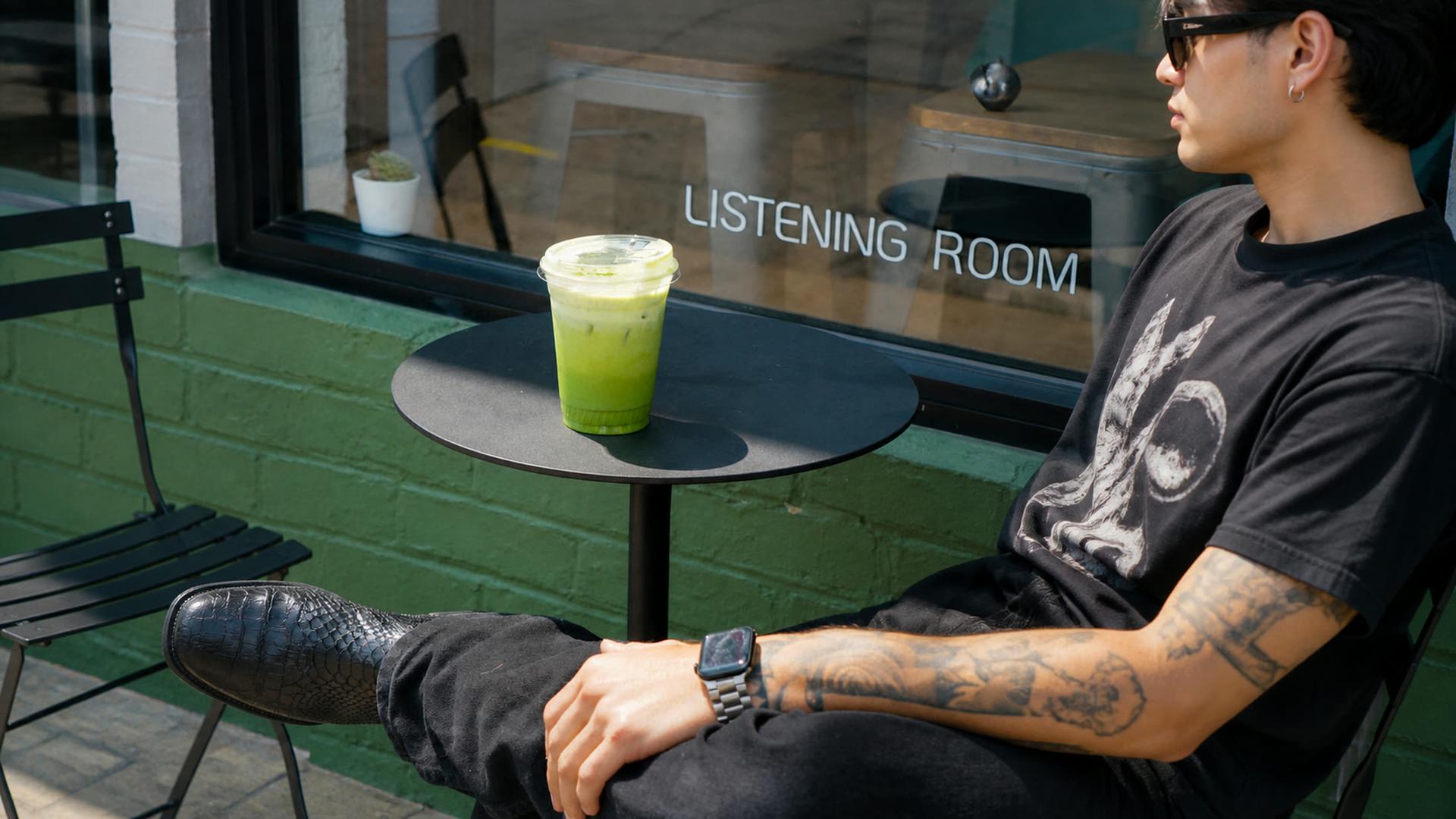 Customer in black tee at the table outside the Listening Room window with iced matcha